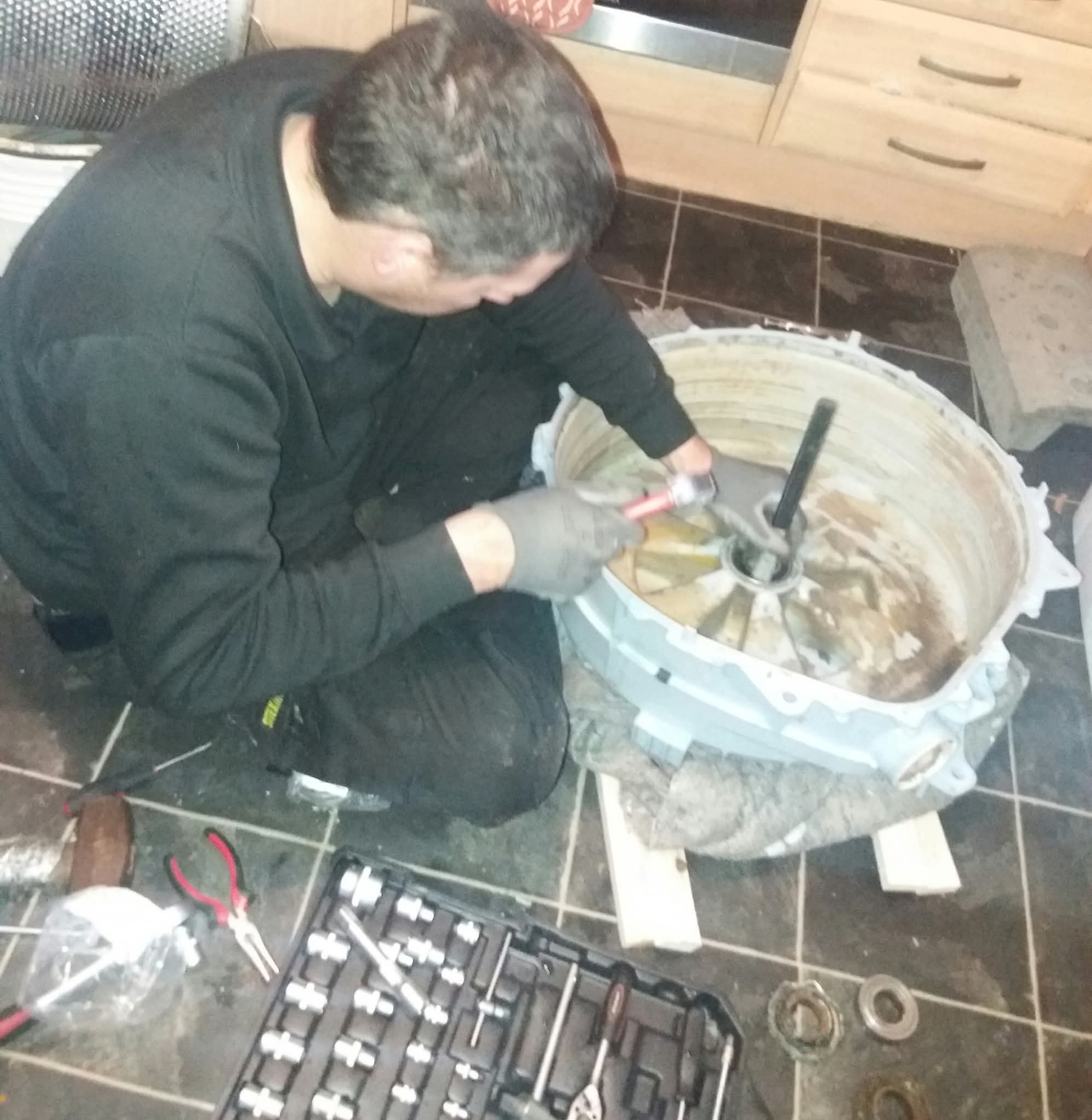 Washing machine drum fully removed for bearing replacement, tools laid out